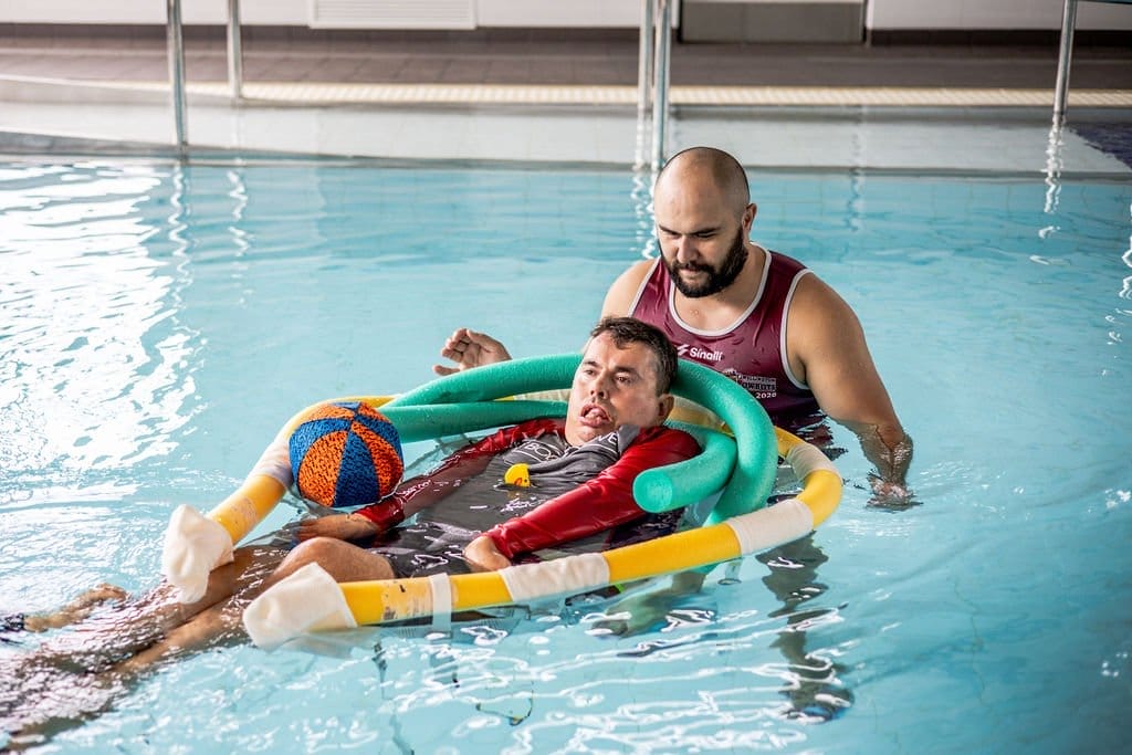 Exercise therapist in a hydrotherapy pool with a disabled participant on a float.